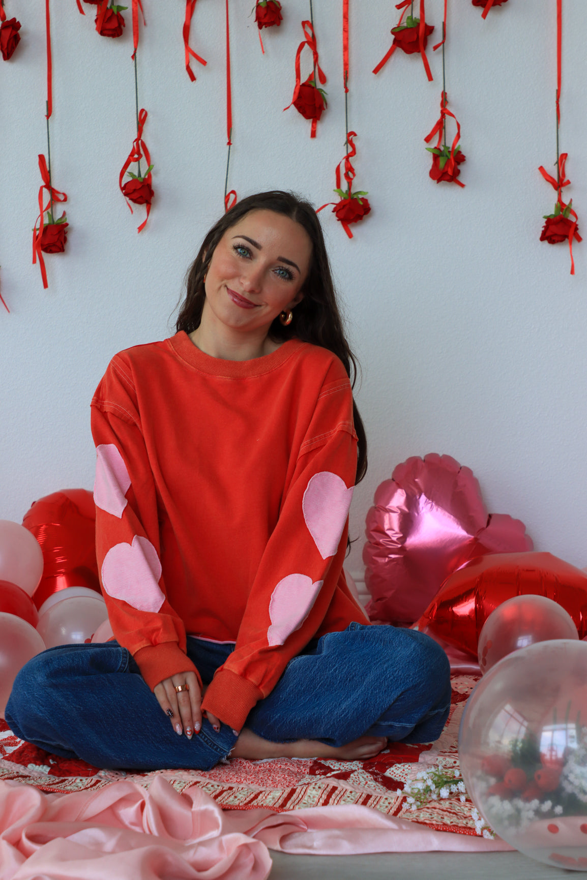 Woman in a red sweater with heart patterns sitting among balloons and decorations.