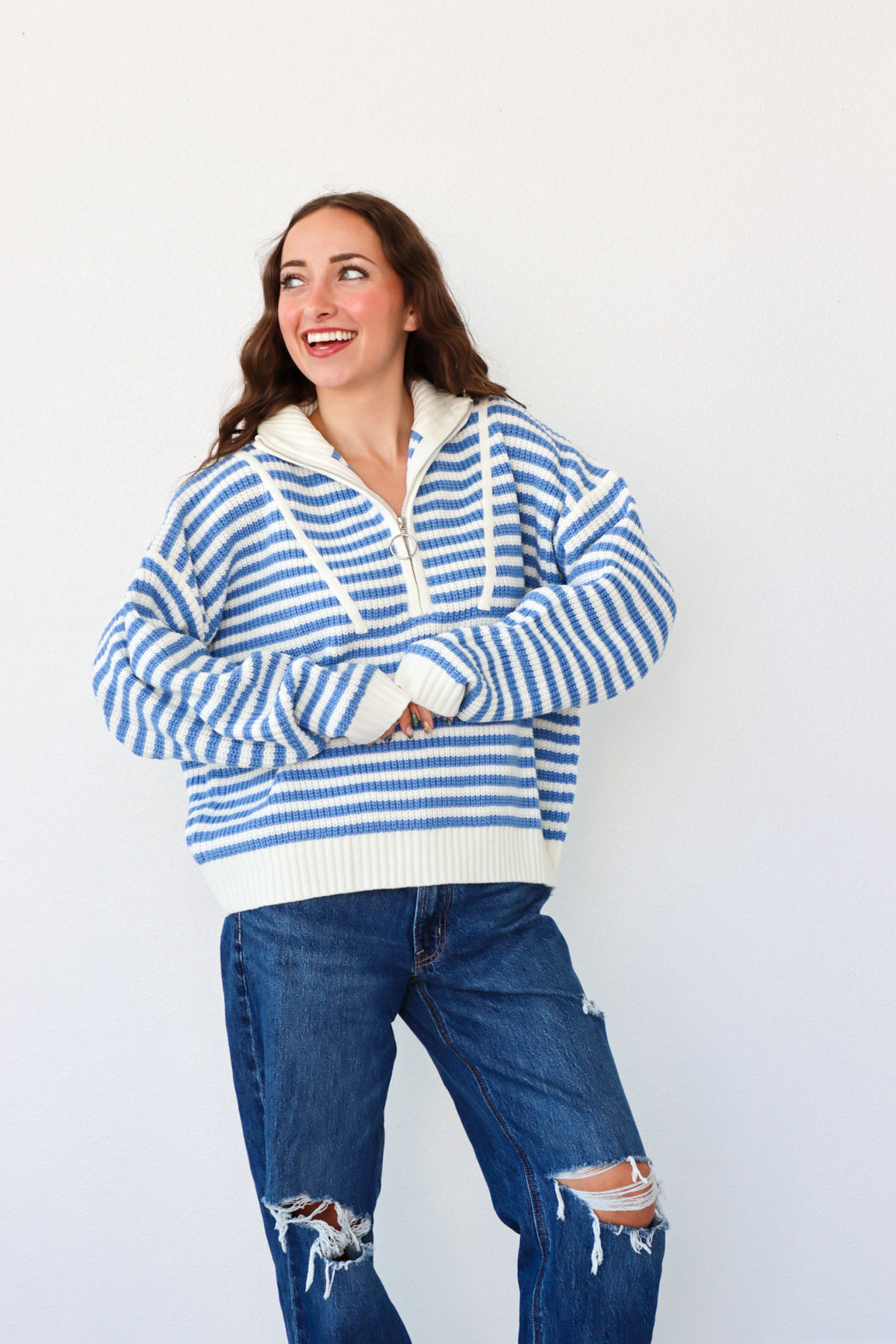 Woman wearing a blue and white striped sweater and ripped jeans on a white background