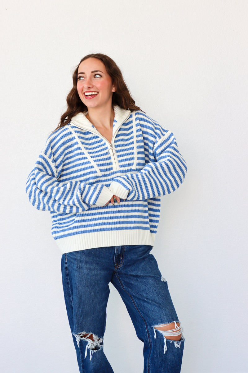 Woman wearing a blue and white striped sweater and ripped jeans on a white background