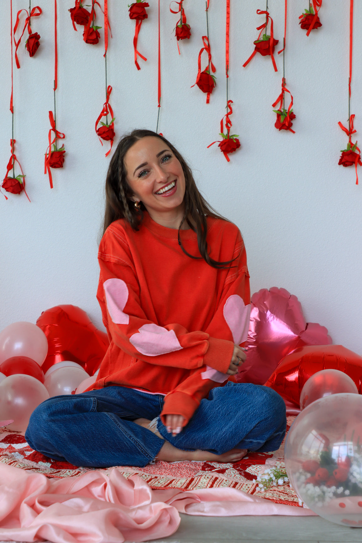 Woman in a red sweater with pink bunny ears surrounded by balloons and decorations on a white wall.