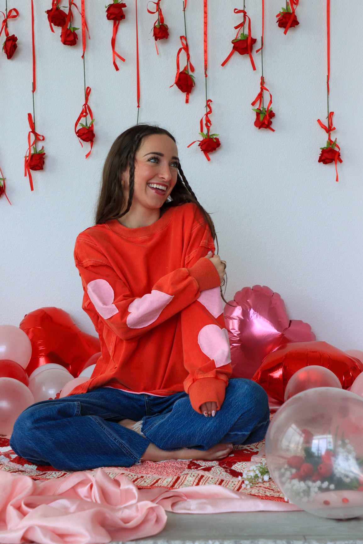 Woman in a red sweater with pink bunny ears sitting among balloons and decorations.