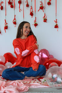 Woman in a red sweater with pink bunny ears sitting among balloons and decorations.