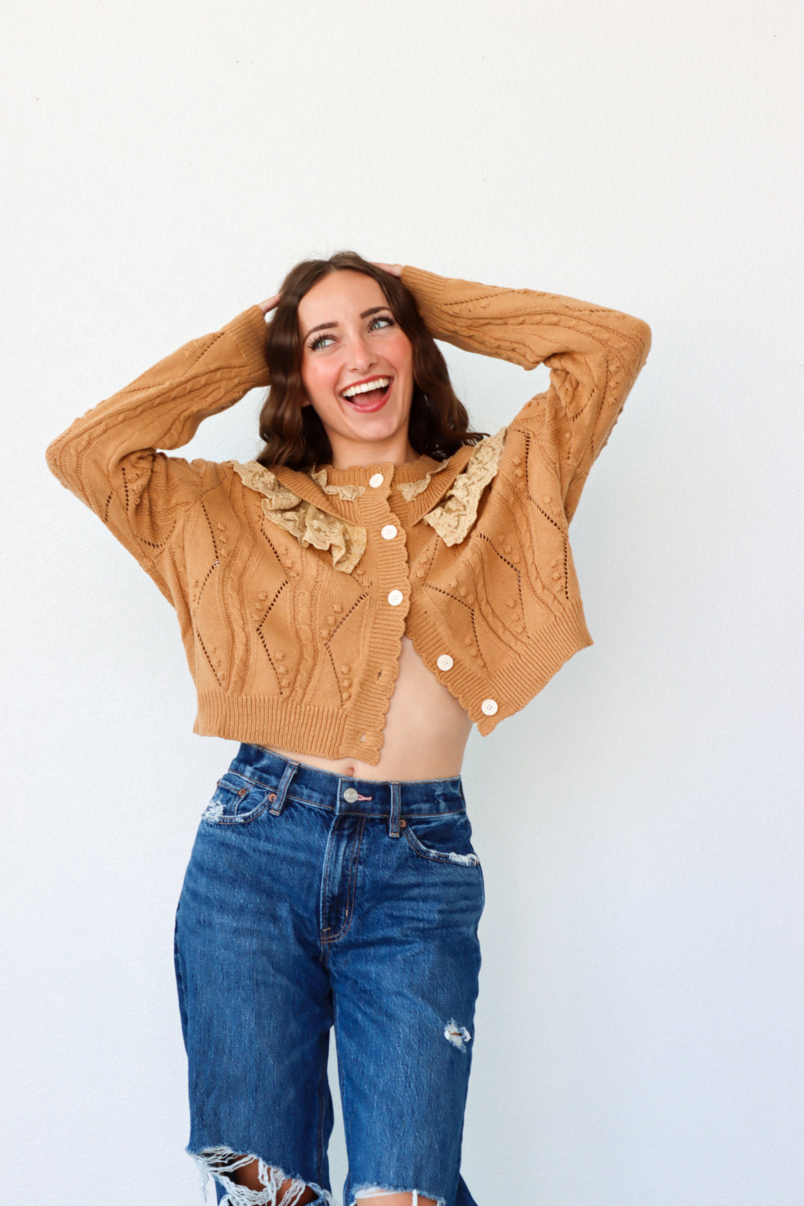 Woman wearing a brown cardigan and blue jeans against a white background