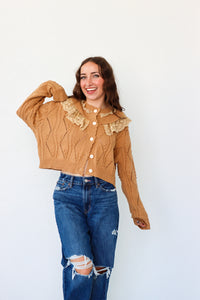 Woman wearing a brown cable knit sweater with lace details and blue jeans on a white background