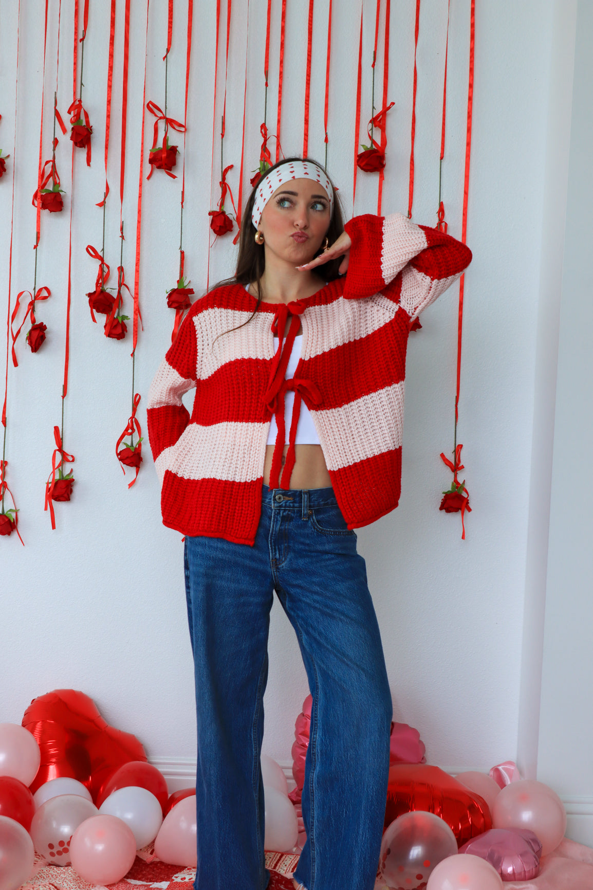 Woman wearing a red and white striped cardigan with hanging decorations and balloons in the background.