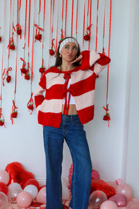 Woman wearing a red and white striped cardigan with hanging decorations and balloons in the background.