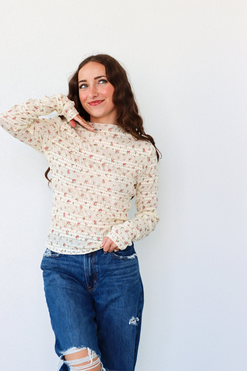 Woman wearing a floral long-sleeve top and blue jeans against a white background