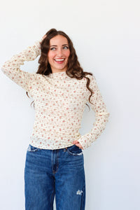 Woman wearing a floral long-sleeve top and blue jeans against a white background