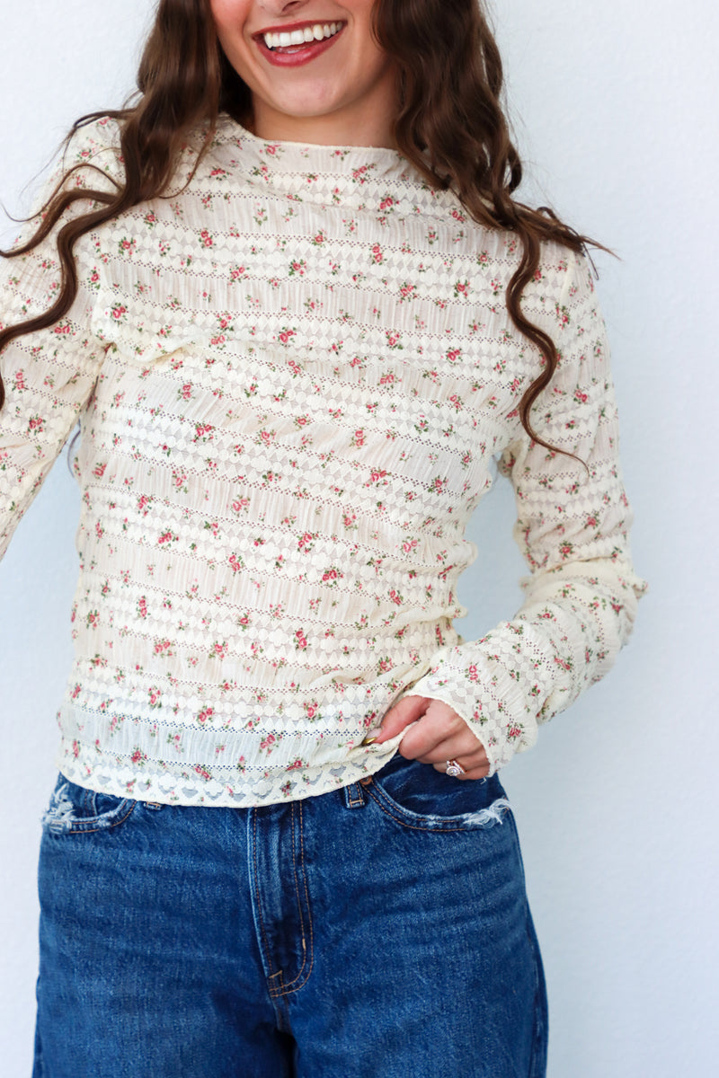 Woman wearing a floral long-sleeve top and blue jeans against a white background