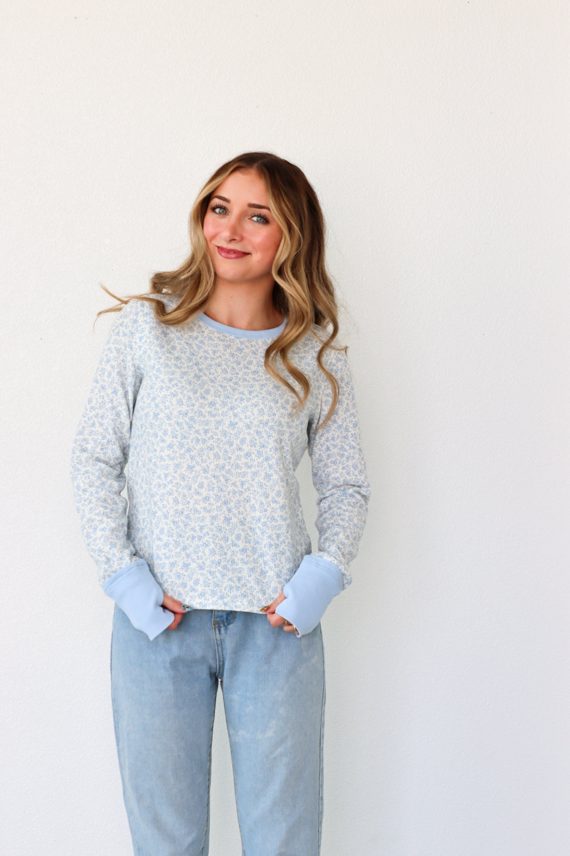 Woman wearing a light gray sweater and light blue jeans against a white background