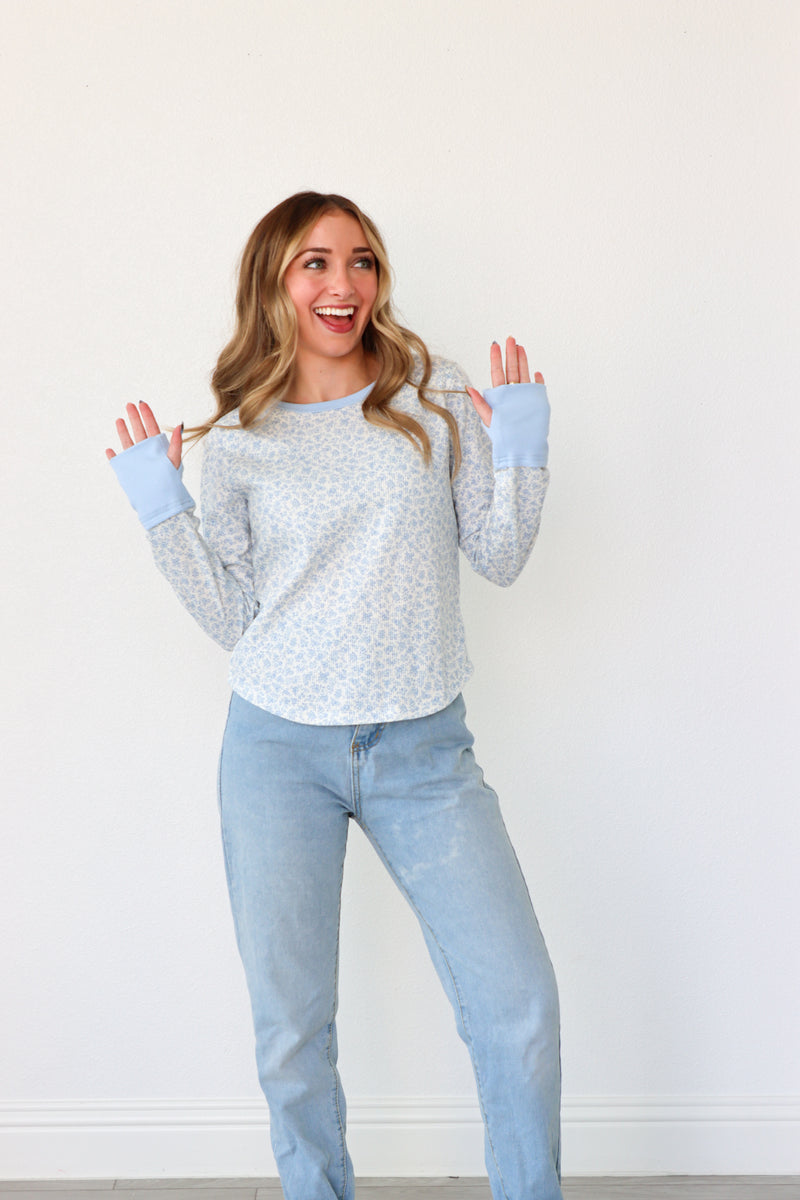 Woman wearing a gray sweater and light blue jeans with matching gloves against a white background