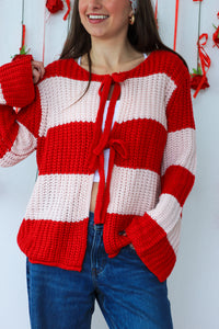 Person wearing a red and white striped sweater with a bow tie, standing against a white background.