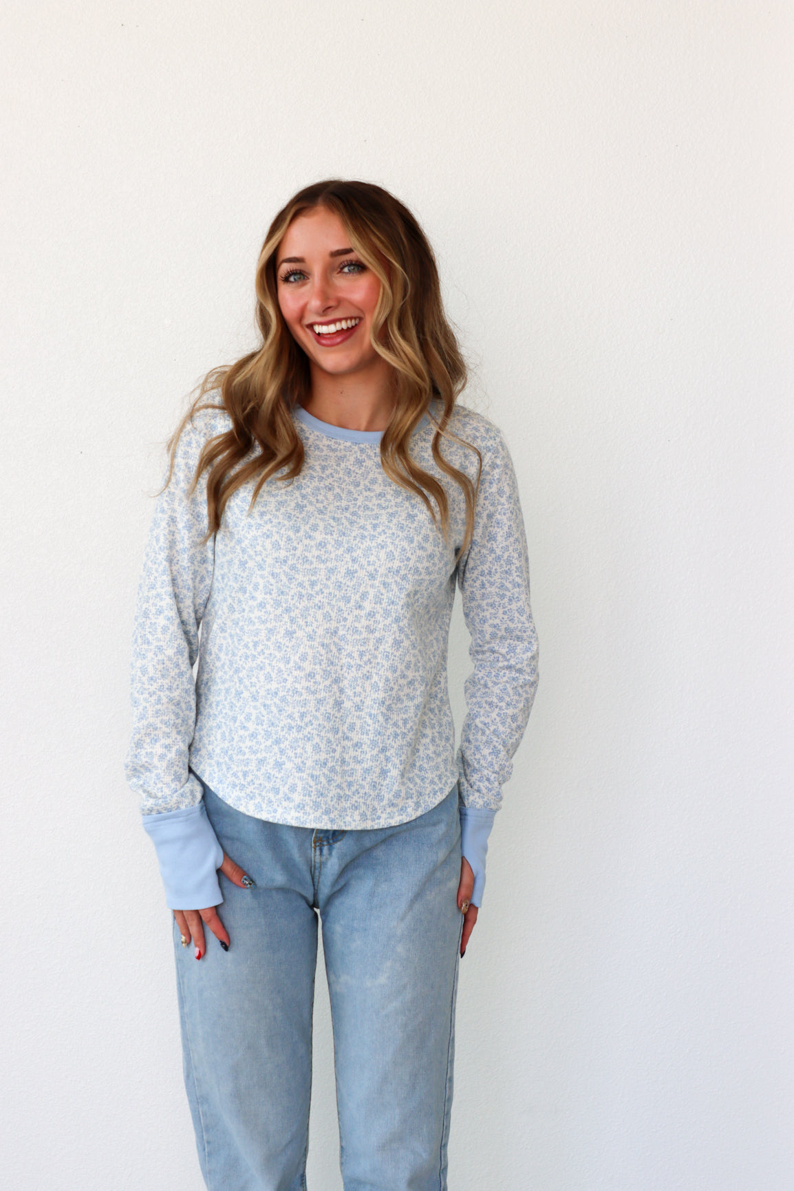 Woman wearing a light blue floral sweater and jeans against a white background
