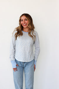 Woman wearing a light blue floral sweater and jeans against a white background