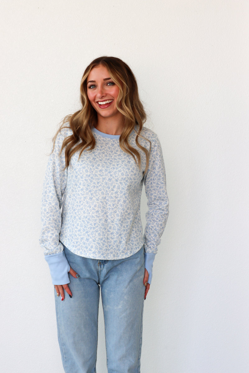 Woman wearing a light blue floral sweater and jeans against a white background