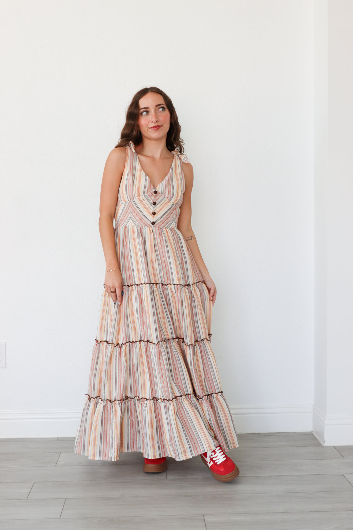 Woman wearing a striped dress with red shoes against a white wall