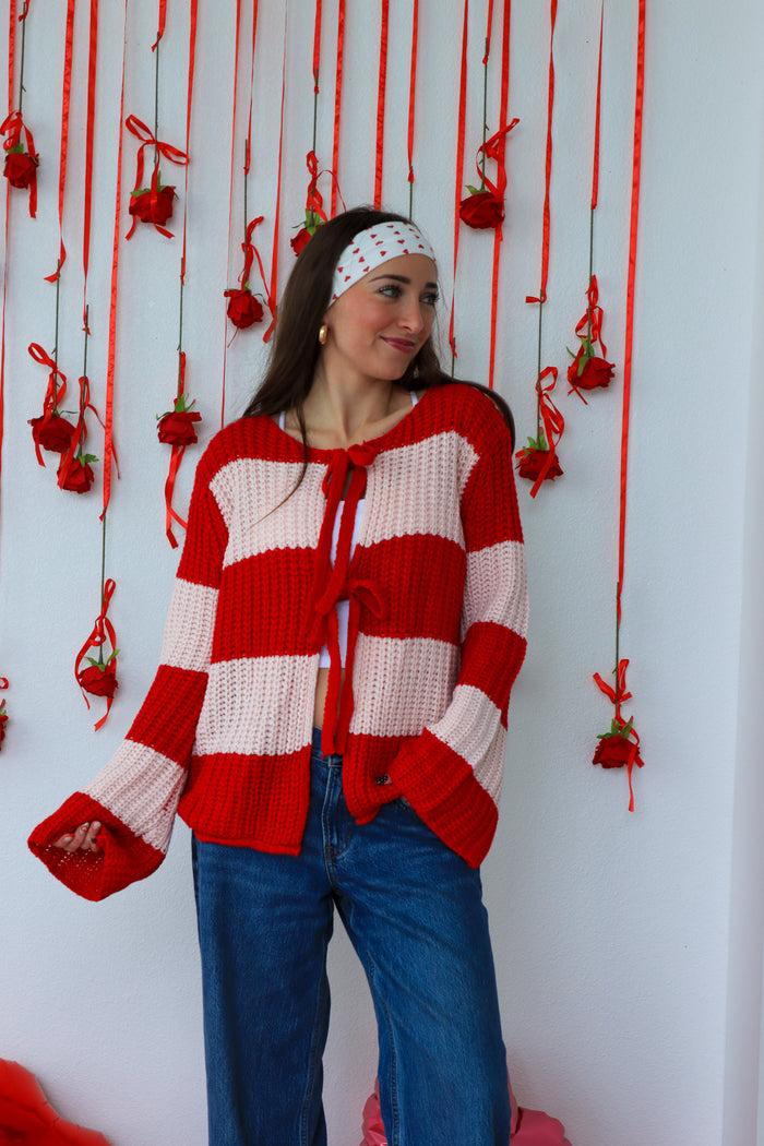 Woman wearing a red and white striped sweater with hanging red decorations on a white wall.