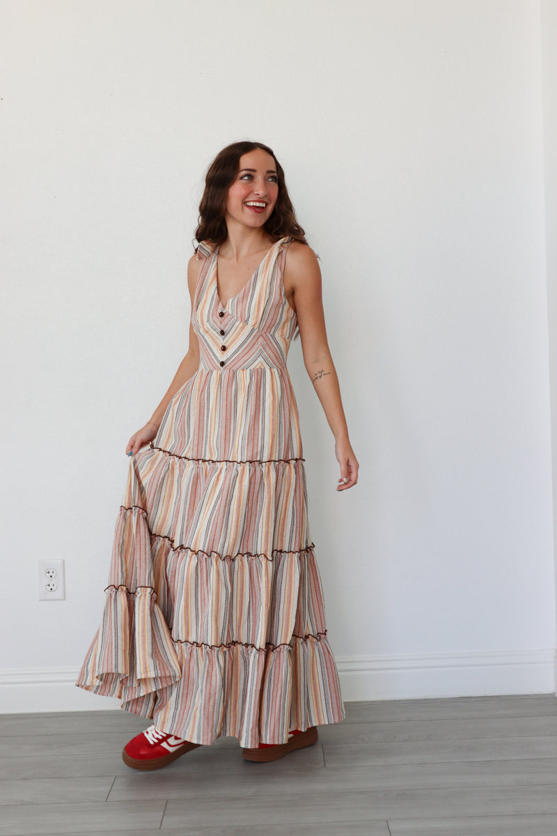 Woman wearing a striped dress with ruffled layers against a white wall.