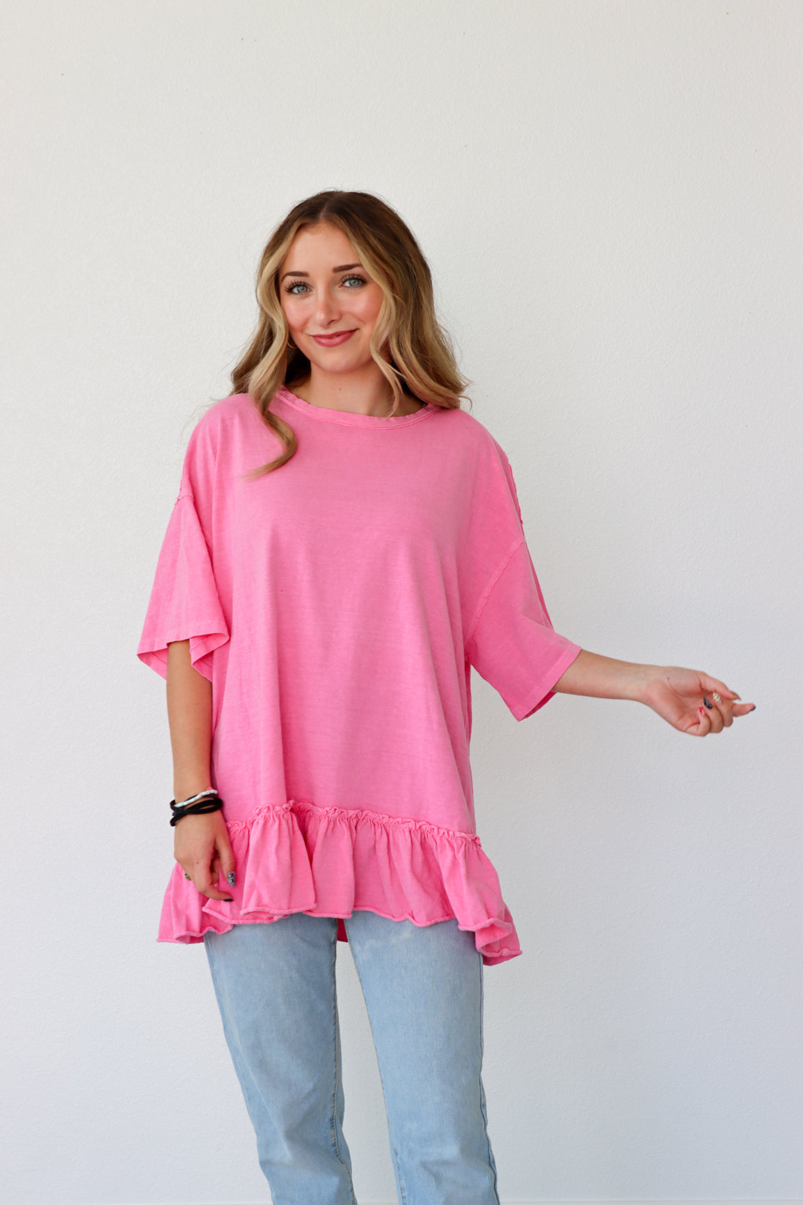 Woman wearing a pink ruffled top and light blue jeans against a white background