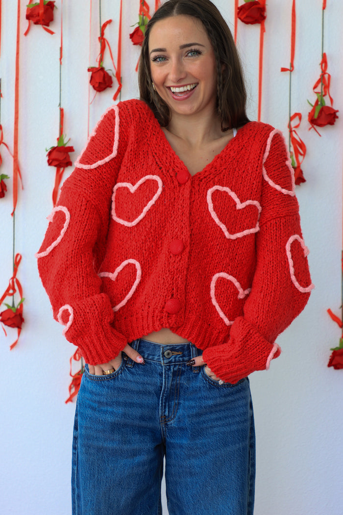 Woman wearing a red sweater with heart patterns against a white background with red ribbons.