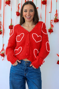 Woman wearing a red cardigan with heart patterns against a decorative background.
