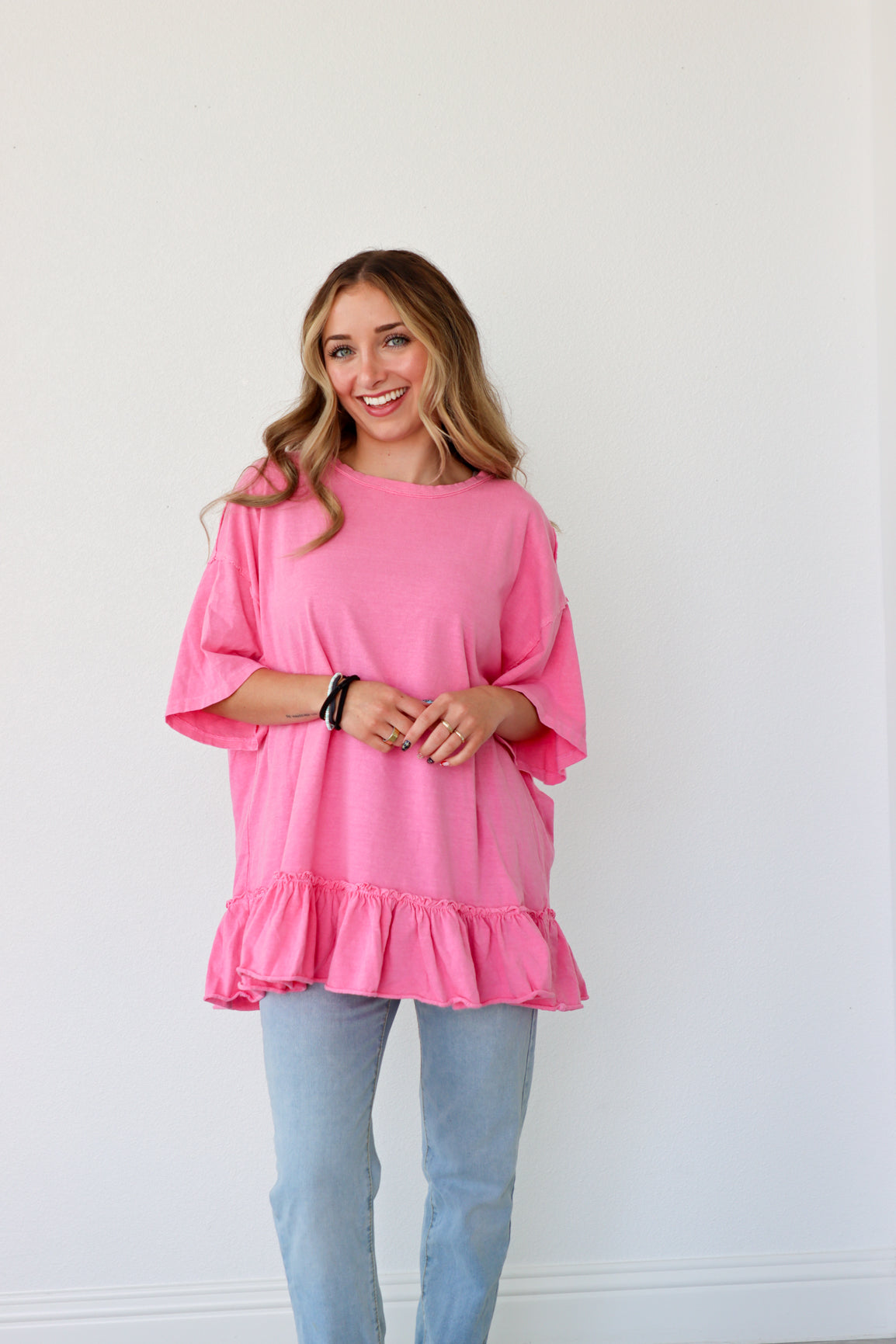 Woman wearing a pink ruffled top and light blue jeans against a white background