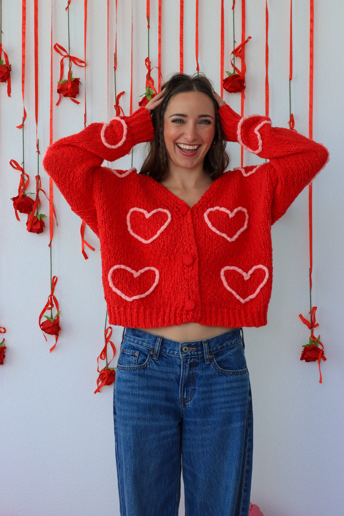Person wearing a red sweater with heart patterns in front of a decorative background.