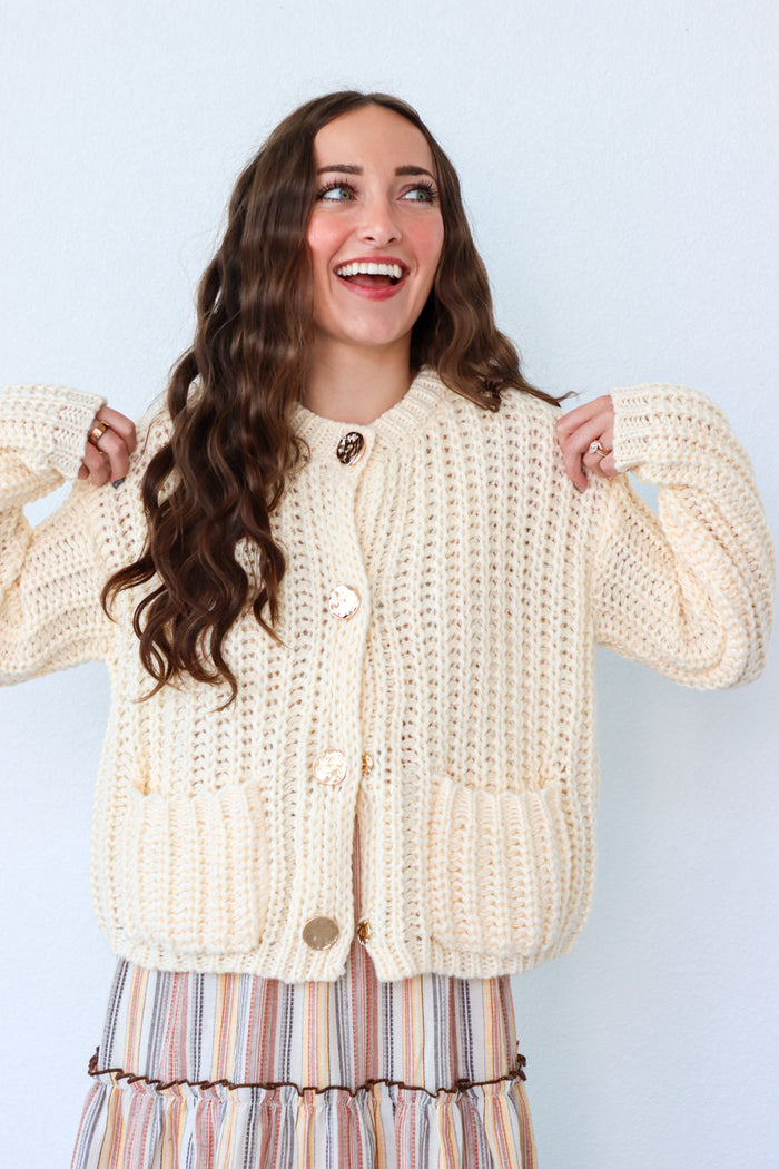 Woman wearing a cream-colored knitted cardigan against a light blue background