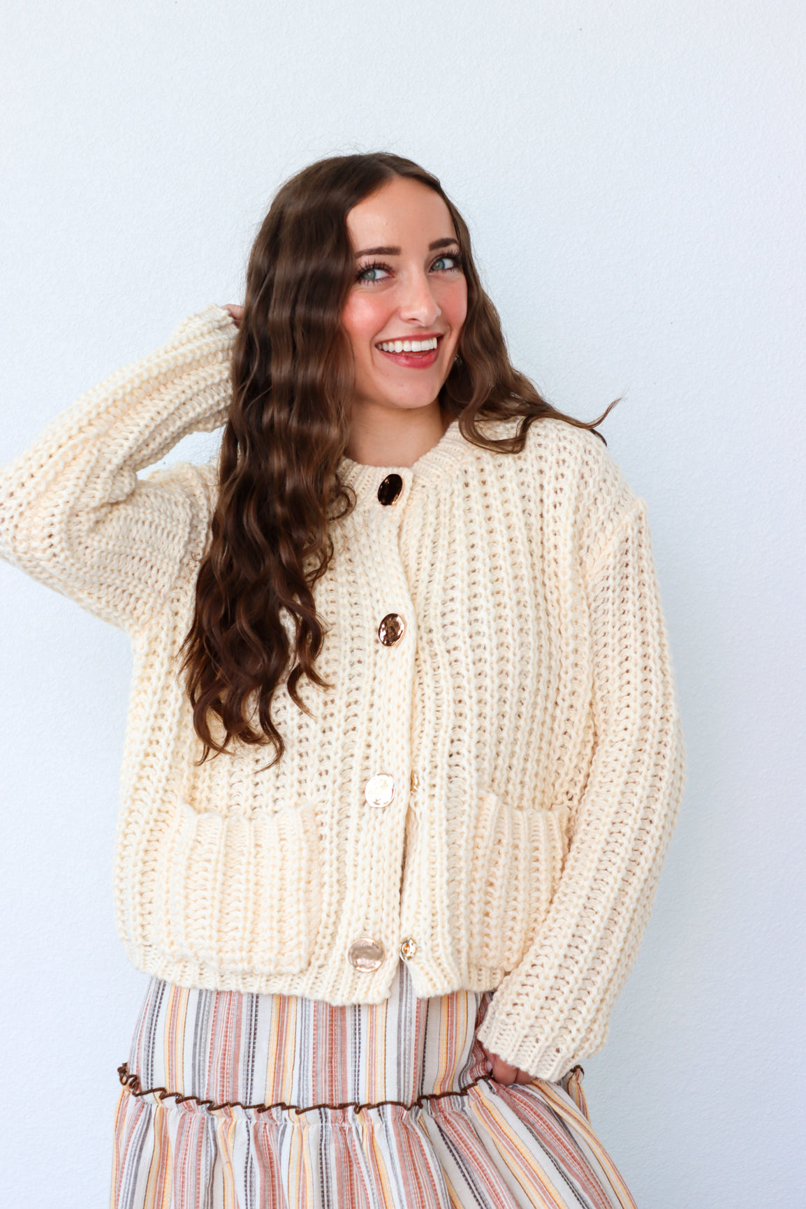 Woman wearing a cream knitted cardigan against a light blue background