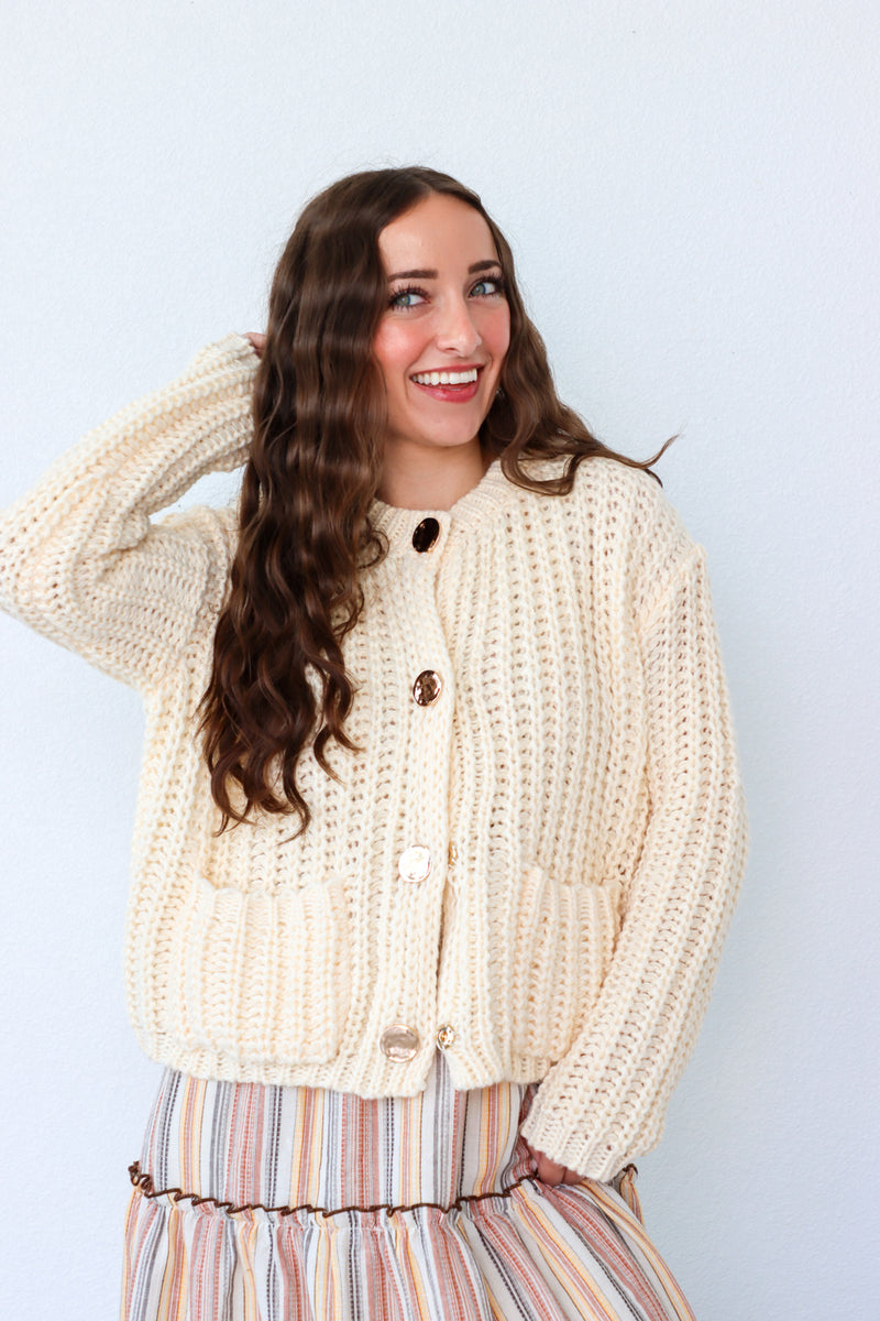 Woman wearing a cream knitted cardigan against a light blue background