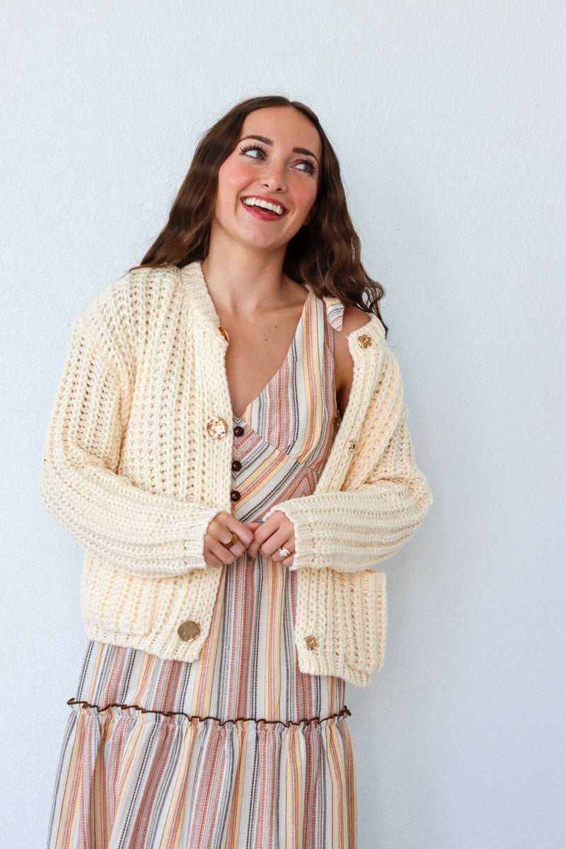 Woman wearing a cream cardigan over a striped dress against a light blue background