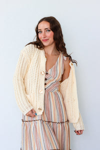 Woman wearing a striped dress with a cream cardigan against a light blue background