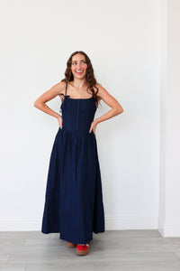 Woman wearing a navy blue dress standing against a white wall.