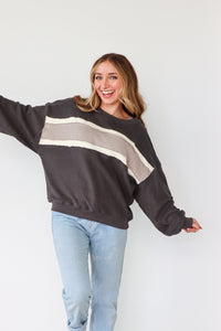 Woman wearing a dark gray sweatshirt with a beige stripe and light blue jeans against a white background