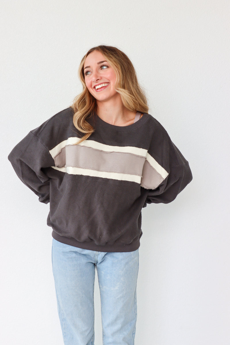 Woman wearing a dark gray sweatshirt with color-blocked design and light blue jeans against a white background