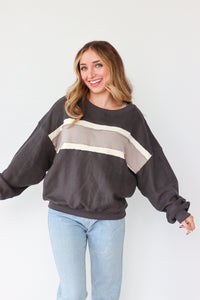 Woman wearing a dark gray sweatshirt with a beige stripe and light blue jeans on a white background