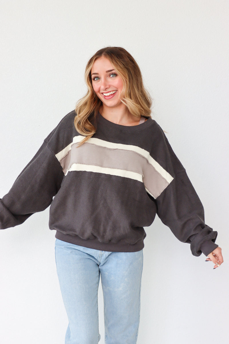 Woman wearing a dark gray sweatshirt with a beige stripe and light blue jeans on a white background
