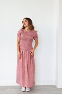 Woman wearing a pink dress standing against a white wall