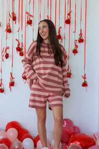 Woman in a pink and white striped outfit standing in front of a decorative wall with red ribbons and balloons.