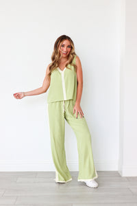 Woman wearing a light green sleeveless top and pants set against a white background