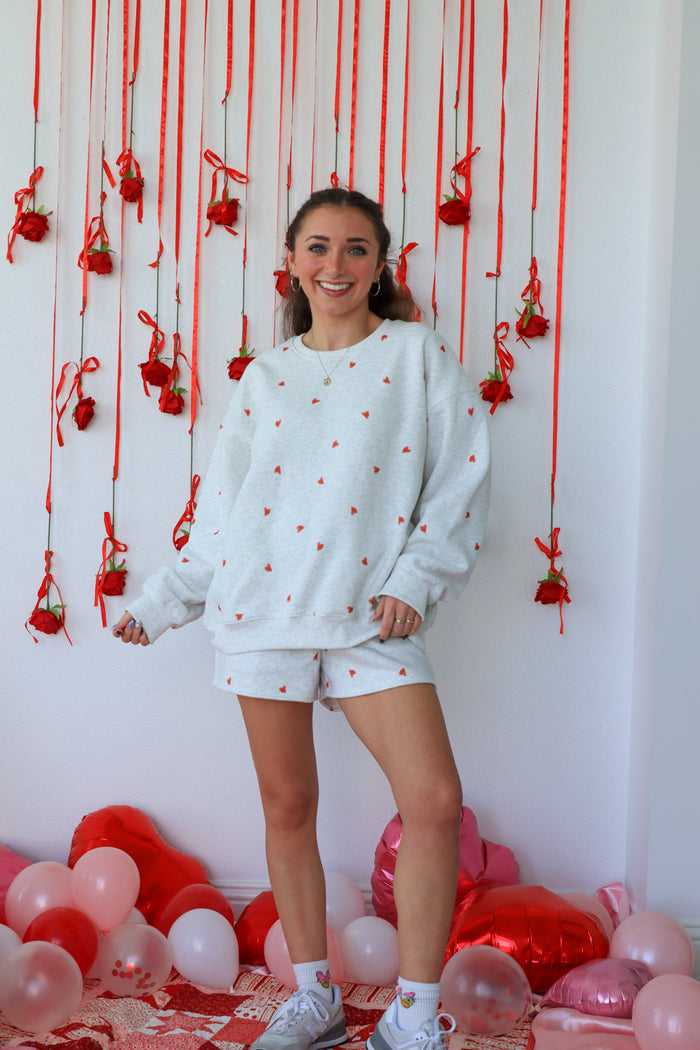 Woman in a white sweatshirt and shorts standing in front of a decorative wall with red strings and balloons.