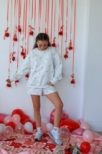 Person in a white polka dot outfit standing in a room decorated with red and pink balloons and streamers.