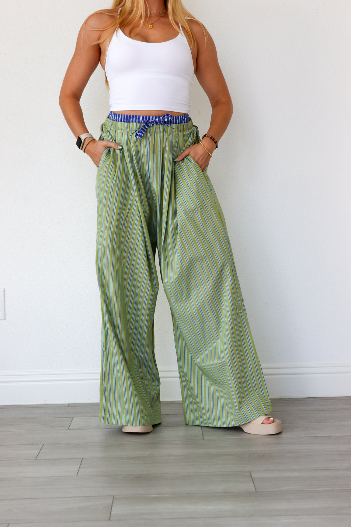 Woman wearing green striped pants and a white top against a white wall.
