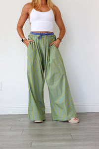 Woman wearing green striped pants and a white top against a white wall.