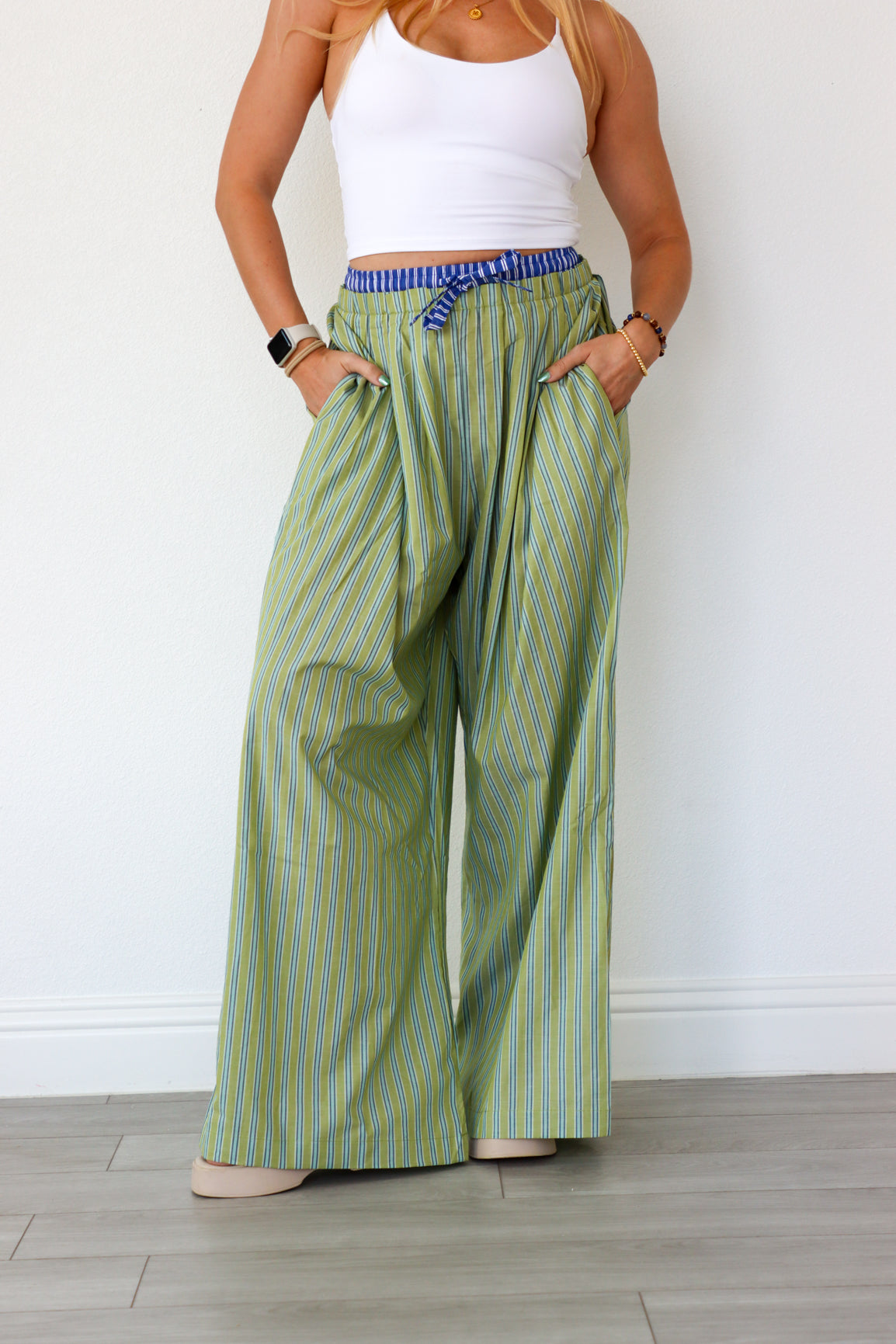 Person wearing green striped wide-leg pants and a white top against a white wall.
