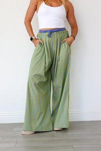 Person wearing green striped wide-leg pants and a white top against a white wall.