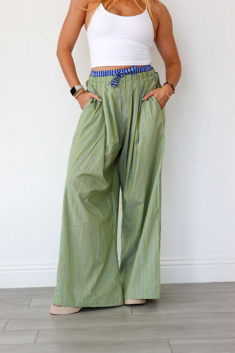 Person wearing green striped wide-leg pants and a white top against a white wall.