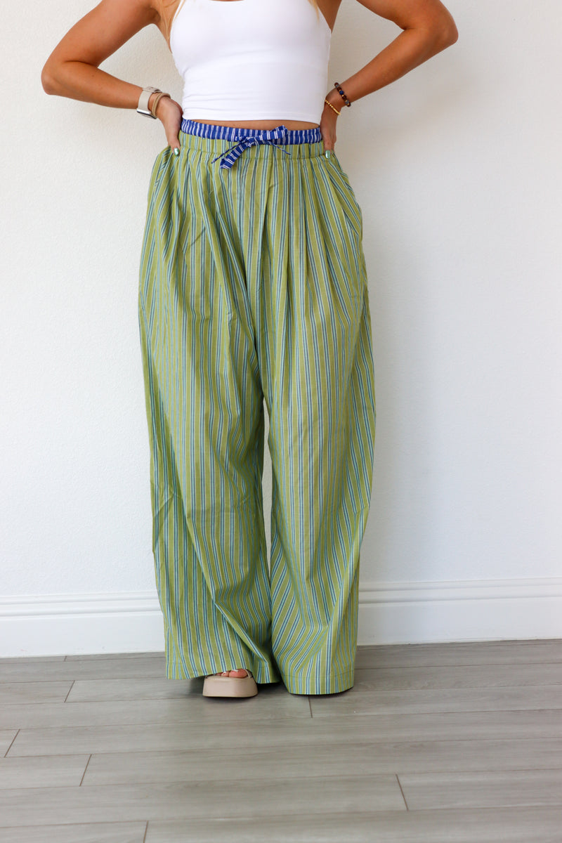 Person wearing green striped pants and a white top against a plain background