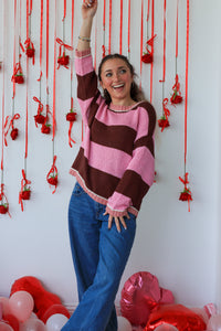 Woman in a striped sweater and blue jeans standing in front of red ribbons and balloons.