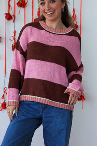 Person wearing a pink and brown striped sweater with blue jeans against a white background.